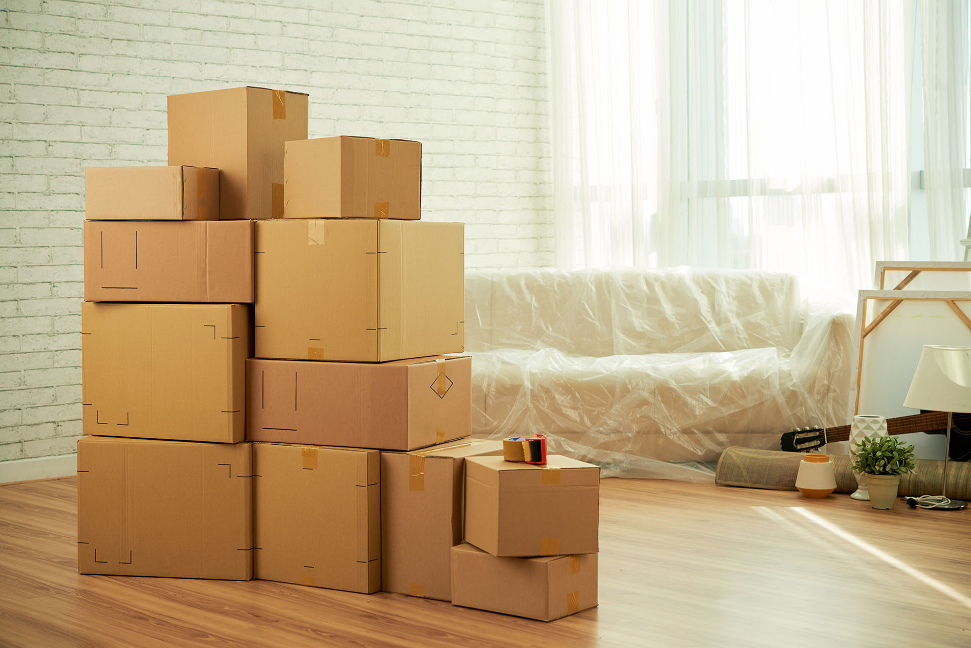 Interior de una sala con cajas de paquetes apiladas en el medio y un sofá cubierto con film.